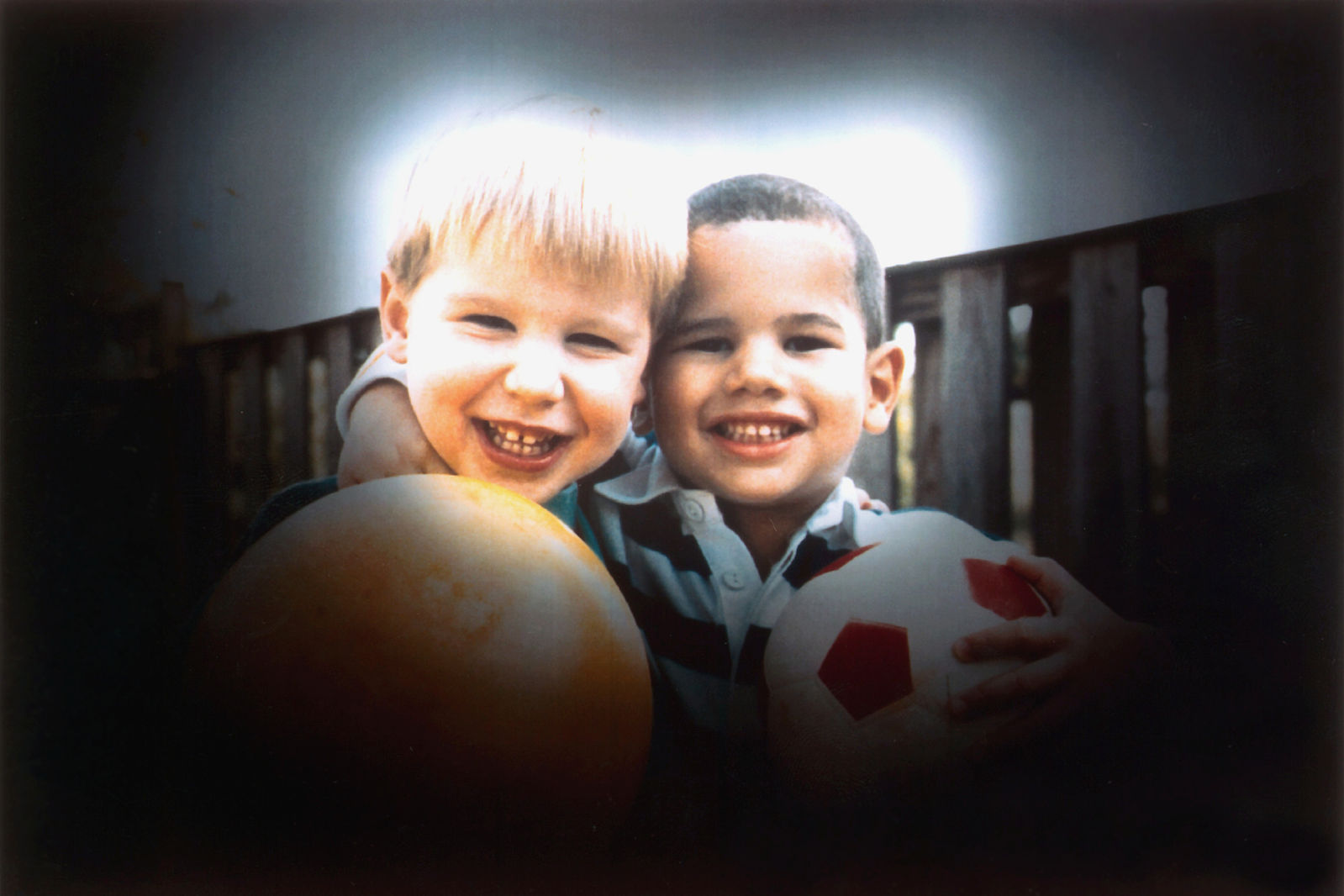 Due bambini sorridenti che si abbracciano; il primo tiene un pallone arancione, mentre l’altro stringe un pallone da calcio bianco con pentagoni rossi. I bordi dell’immagine sono scuriti per simulare la visione ristretta tipica del glaucoma